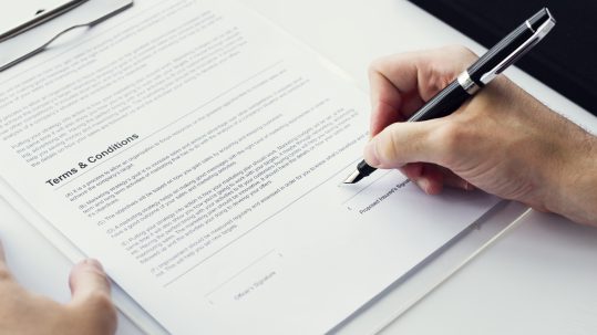 Closeup of hand signing paper workspace